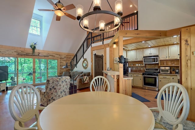 dining room featuring ceiling fan with notable chandelier, light wood-type flooring, and high vaulted ceiling