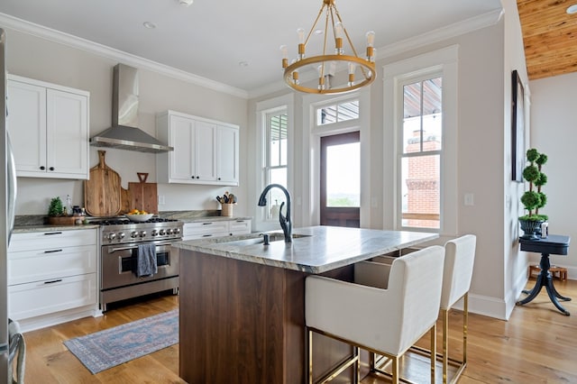 kitchen featuring a sink, white cabinetry, high end stainless steel range, wall chimney exhaust hood, and an island with sink