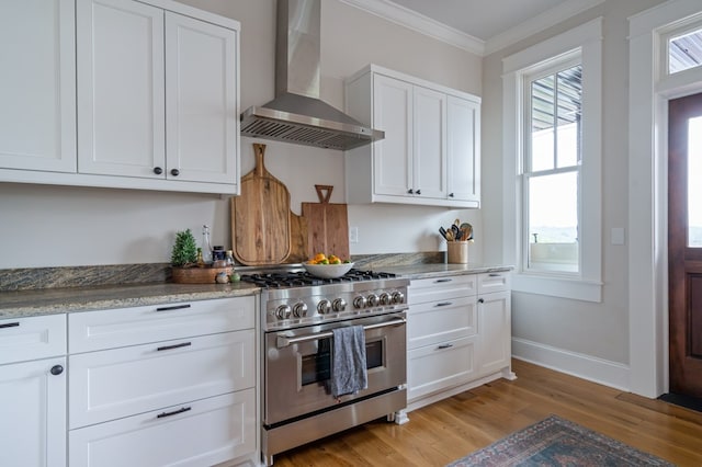 kitchen with wall chimney exhaust hood, high end stainless steel range, light stone countertops, crown molding, and white cabinetry