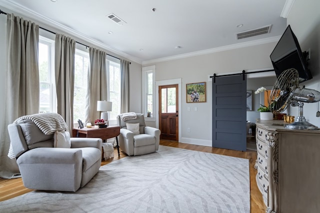 living area with a barn door, light wood-type flooring, visible vents, and crown molding