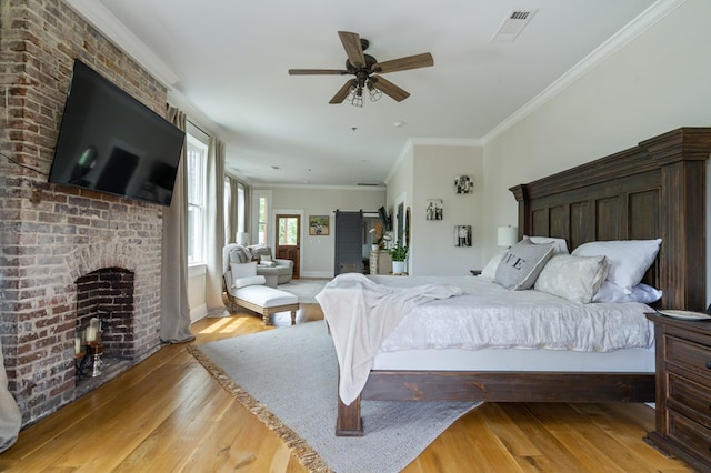 bedroom with a fireplace, visible vents, a barn door, ornamental molding, and light wood-type flooring