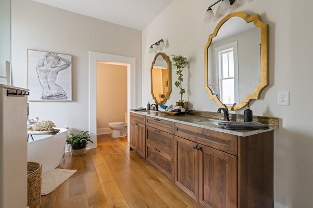 full bathroom featuring double vanity, a soaking tub, toilet, a sink, and wood finished floors