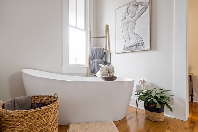 bathroom featuring a soaking tub, baseboards, and wood finished floors