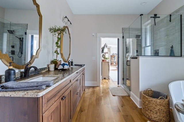 full bathroom featuring double vanity, a stall shower, a sink, wood finished floors, and baseboards