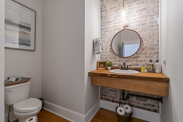 half bath with baseboards, a sink, toilet, and wood finished floors