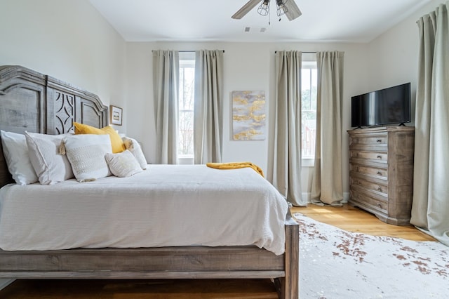 bedroom featuring light wood finished floors, multiple windows, visible vents, and a ceiling fan