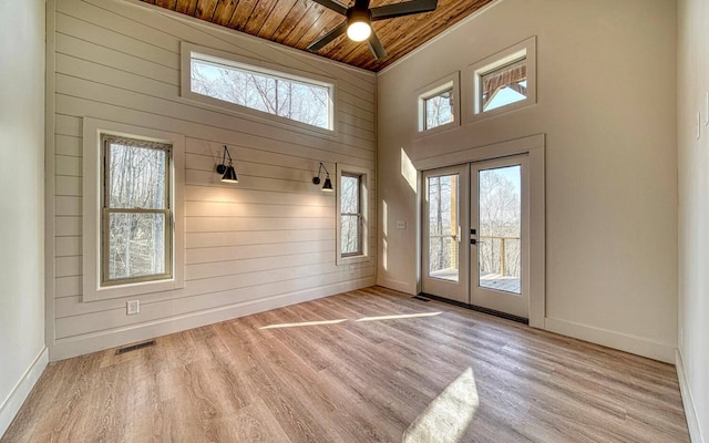 interior space featuring french doors, wooden walls, light wood-type flooring, a towering ceiling, and wood ceiling