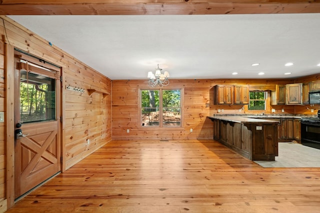 kitchen with kitchen peninsula, black appliances, a chandelier, light hardwood / wood-style floors, and wood walls