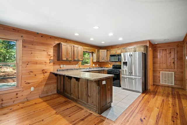 kitchen featuring wood walls, black appliances, sink, light wood-type flooring, and kitchen peninsula