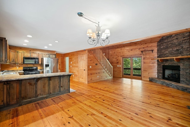 kitchen with kitchen peninsula, sink, black appliances, light hardwood / wood-style floors, and wood walls