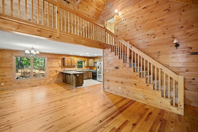 stairs featuring wooden walls, high vaulted ceiling, wood-type flooring, and a notable chandelier