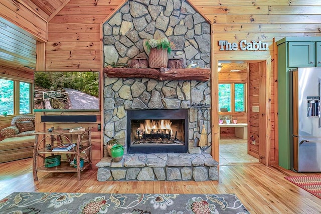 living room with light hardwood / wood-style floors, wood ceiling, high vaulted ceiling, a stone fireplace, and wooden walls