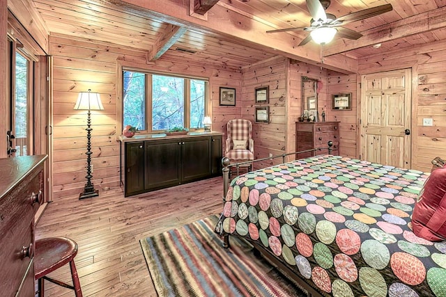 bedroom with ceiling fan, beamed ceiling, light wood-type flooring, and wood walls