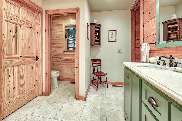 bathroom with tile patterned floors, wood walls, vanity, and toilet