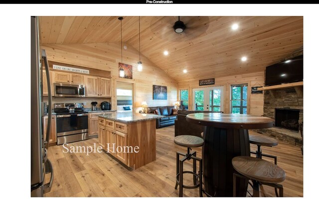 kitchen featuring wood walls, hanging light fixtures, a center island, light stone counters, and stainless steel appliances