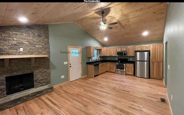 kitchen with a stone fireplace, sink, light wood-type flooring, appliances with stainless steel finishes, and ceiling fan