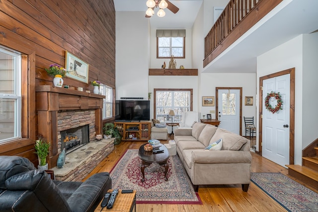 living room featuring ceiling fan, a fireplace, a high ceiling, and light wood-type flooring