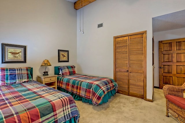 carpeted bedroom featuring beamed ceiling, a high ceiling, and a closet