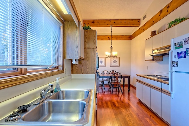 kitchen featuring sink, wood-type flooring, hanging light fixtures, white fridge, and white cabinets