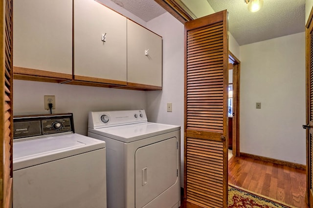 laundry room with cabinets, hardwood / wood-style flooring, a textured ceiling, and washer and clothes dryer