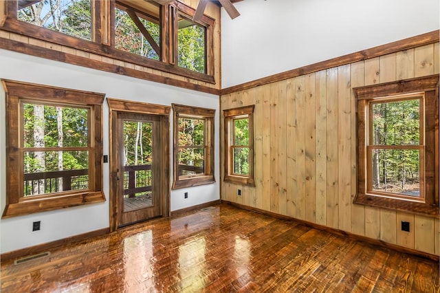 interior space with high vaulted ceiling, ceiling fan, and wood walls