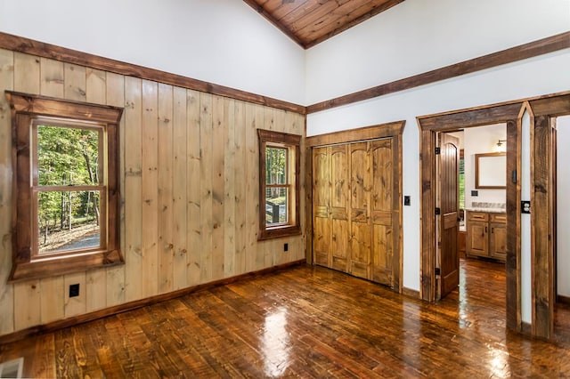 unfurnished bedroom with connected bathroom, wooden ceiling, dark hardwood / wood-style flooring, vaulted ceiling, and wooden walls