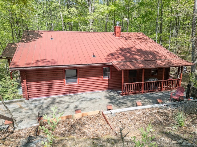 exterior space featuring a standing seam roof, log siding, a chimney, and metal roof