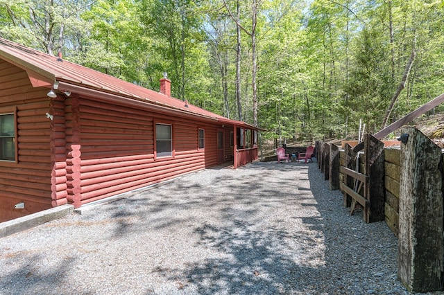 view of side of home with a view of trees, log siding, a chimney, and metal roof