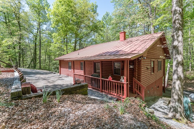 back of house with a chimney, a standing seam roof, log exterior, metal roof, and a porch