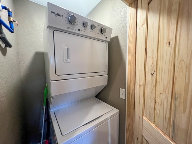 washroom with stacked washing maching and dryer, a textured wall, and laundry area
