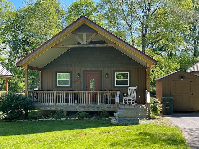 view of front of house with covered porch, a storage unit, an outbuilding, a front lawn, and board and batten siding