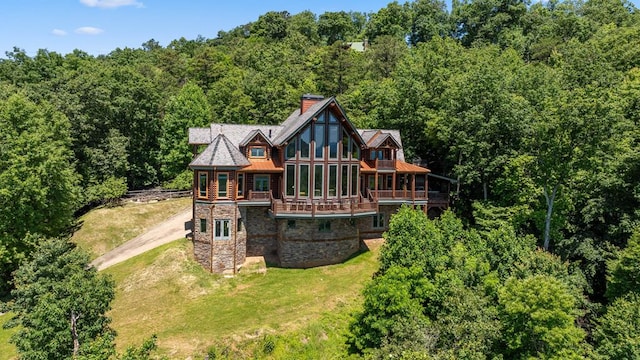 exterior space featuring a yard, stone siding, a wooded view, and a chimney