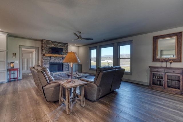 living room with crown molding, ceiling fan, a stone fireplace, and dark hardwood / wood-style flooring