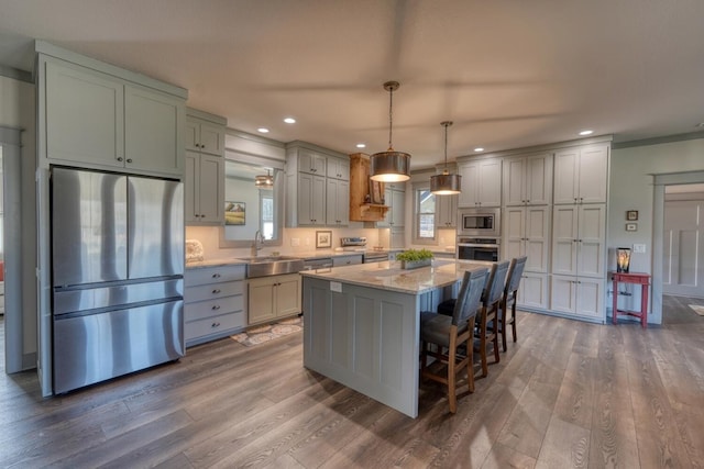 kitchen featuring a kitchen island, appliances with stainless steel finishes, decorative light fixtures, sink, and light stone counters