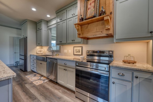 kitchen with appliances with stainless steel finishes, sink, dark wood-type flooring, and light stone counters