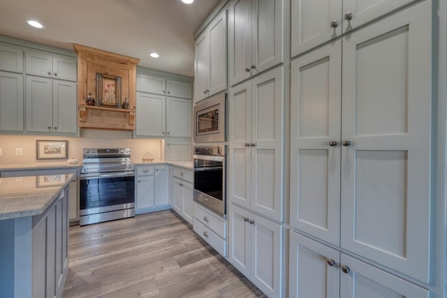 kitchen with appliances with stainless steel finishes, light stone countertops, and light hardwood / wood-style floors