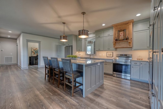 kitchen featuring stainless steel range with electric cooktop, light stone counters, a kitchen island, pendant lighting, and hardwood / wood-style floors