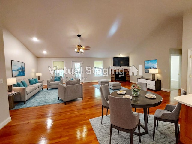 dining room with hardwood / wood-style floors, ceiling fan, a fireplace, and high vaulted ceiling