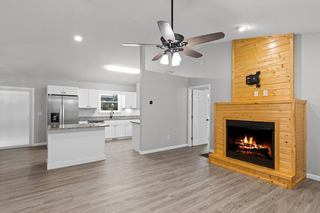 interior space with a ceiling fan, stainless steel refrigerator with ice dispenser, a sink, open floor plan, and white cabinetry