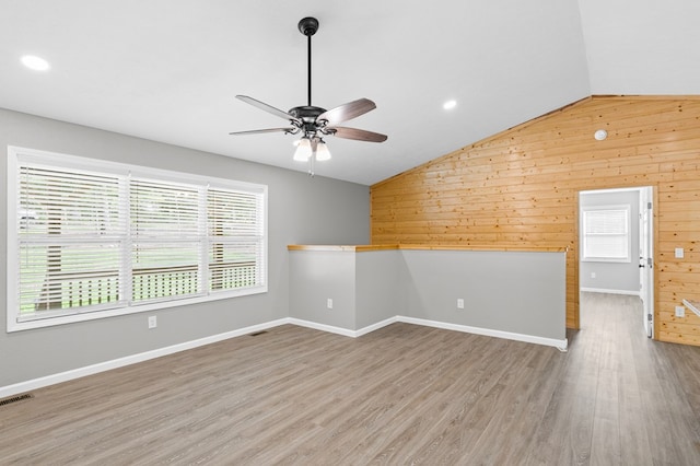 unfurnished room with ceiling fan, vaulted ceiling, wood walls, and visible vents