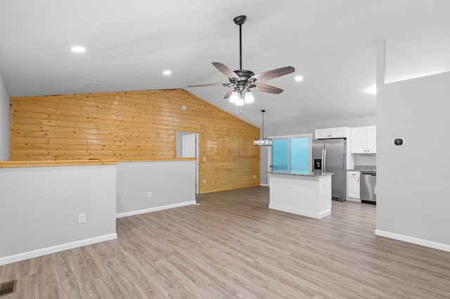 unfurnished living room with baseboards, a ceiling fan, wooden walls, and vaulted ceiling