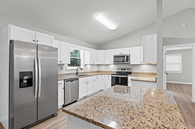 kitchen with appliances with stainless steel finishes, vaulted ceiling, light stone counters, white cabinets, and light wood finished floors