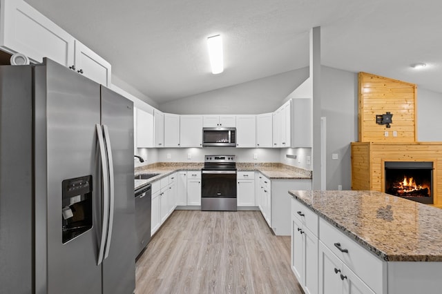 kitchen with light stone countertops, appliances with stainless steel finishes, a sink, light wood finished floors, and lofted ceiling