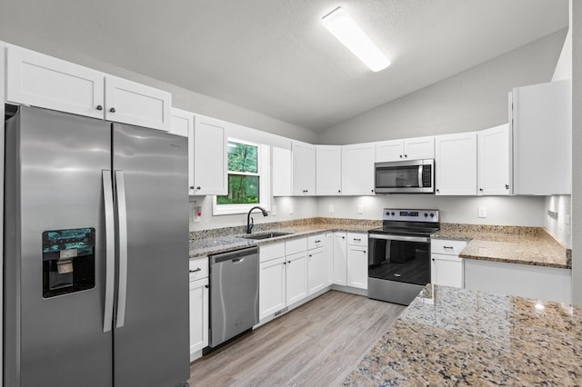 kitchen with lofted ceiling, white cabinetry, light stone counters, a sink, and stainless steel appliances