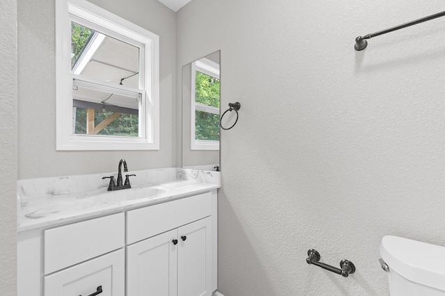 bathroom featuring vanity, a textured wall, and toilet