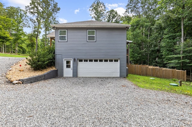 view of side of home with a garage, fence, a shingled roof, and gravel driveway