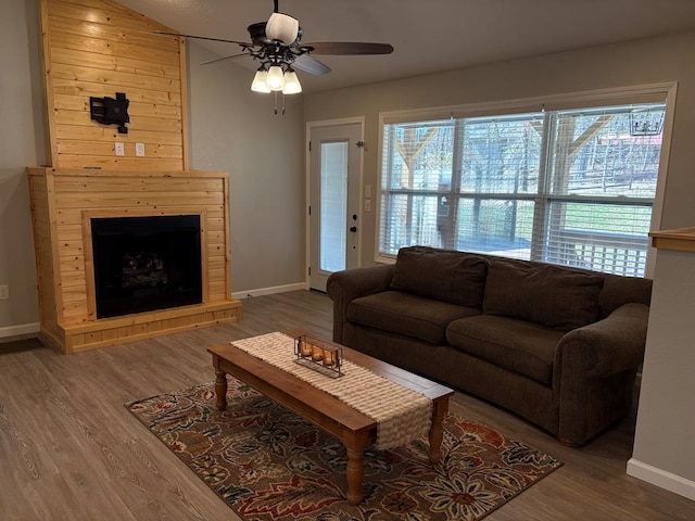 living area featuring baseboards, a fireplace with raised hearth, ceiling fan, and wood finished floors