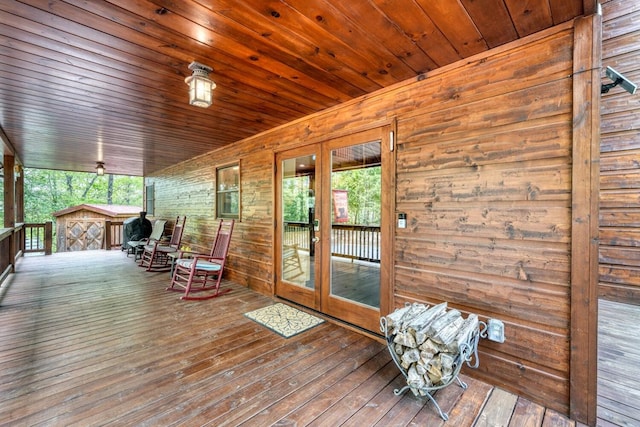 wooden terrace with an outdoor structure, a storage shed, and french doors