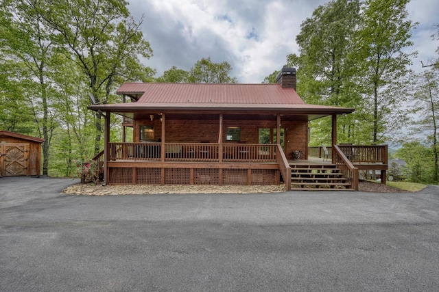view of front facade featuring covered porch, a chimney, and metal roof