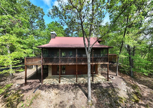 back of property with a chimney, metal roof, a deck, a sunroom, and stone siding